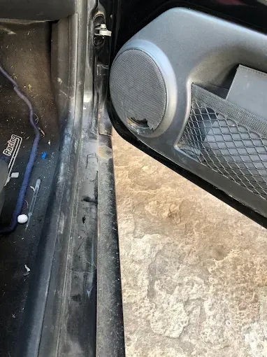 Primer plano del altavoz de la puerta de un coche y su panel interior junto a una superficie de hormigón.
