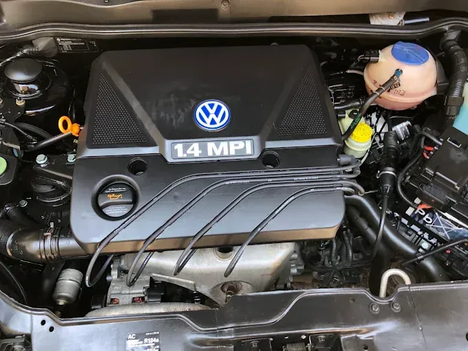 Compartimento del motor Volkswagen 1.4 MPI con cubierta negra y mangueras y depósito de fluidos visibles.