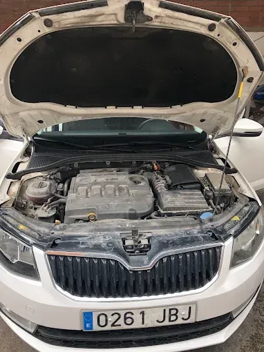 Coche blanco con el capó abierto, dejando ver el compartimento del motor y la parrilla delantera.