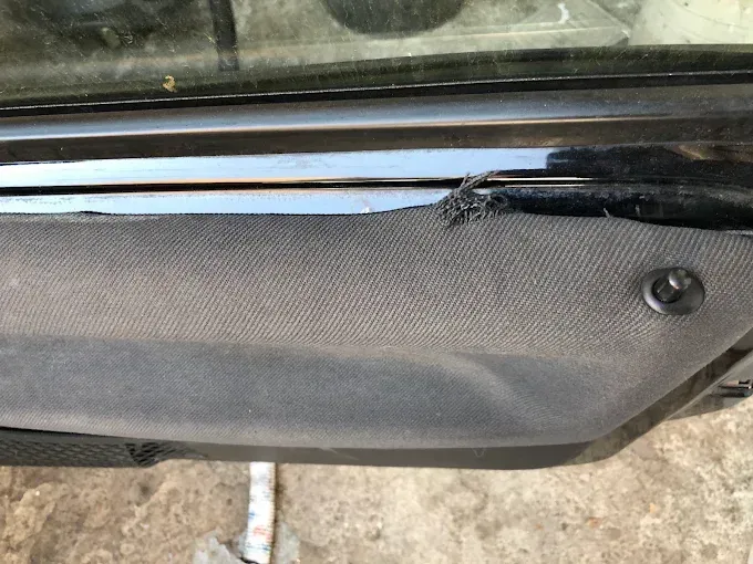 Primer plano de un panel interior de puerta de automóvil negro texturizado con un borde roto cerca de la ventana.