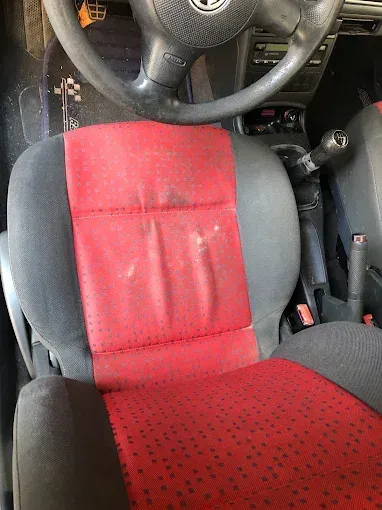 Interior del coche con fundas de asientos negras y rojas y un volante visible por encima del asiento del conductor.
