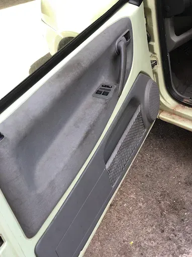 Interior del coche con la puerta abierta, panel gris y altavoz, que se muestra junto al asiento delantero.