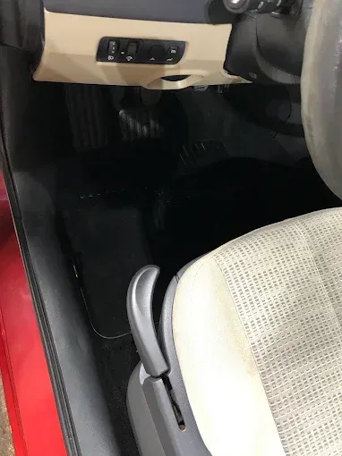 Interior de un coche con salpicadero de color beige, alfombrilla negra y un asiento gris claro en primer plano.