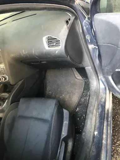 Interior del coche con el asiento del pasajero delantero, la puerta abierta y el panel lateral rayado 