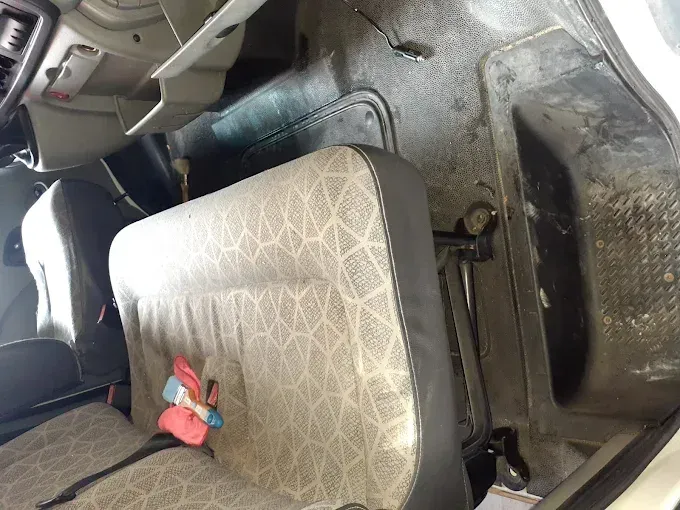 Interior del coche con asiento estampado, elemento rojo en el asiento y alfombrilla en el suelo junto a la consola central.