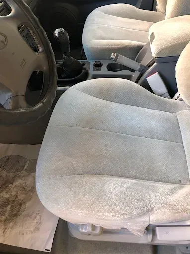 Interior del coche con asientos delanteros de tela beige, volante y consola central visibles.