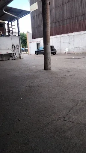 Terreno industrial vacío con un pilar de hormigón, un vehículo estacionado y altos muros de almacén.