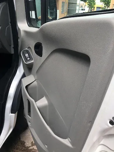 Primer plano del interior de la puerta de un coche gris con un altavoz, una manija y un bolsillo de almacenamiento 