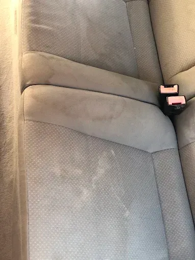 Tapicería gris para asiento de coche con costura visible y hebilla roja del cinturón de seguridad en el lado derecho.