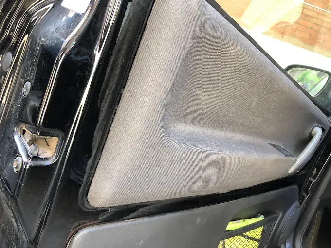 Primer plano del interior de la puerta de un coche con una visera parasol de tela gris y detalles en negro.