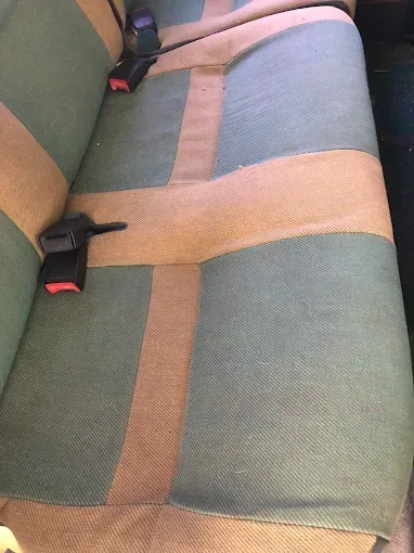 Silla de coche con tapicería de tela multicolor y dos hebillas de cinturón de seguridad negras.