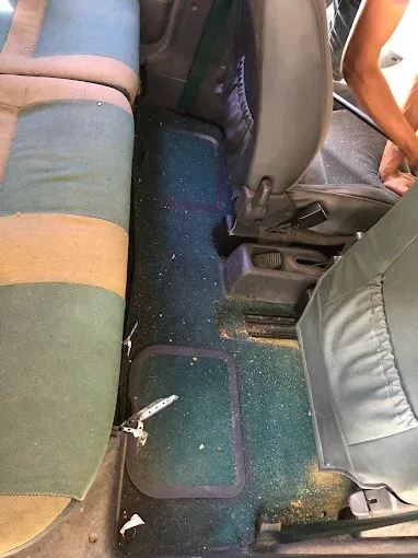 Pasillo de autobús con asientos estampados y suelo alfombrado, donde se aprecia basura cerca del centro.
