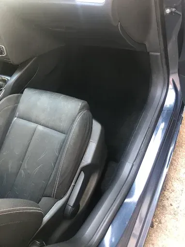 Asiento de coche de cuero negro con la puerta abierta, que deja ver el interior de un vehículo azul.