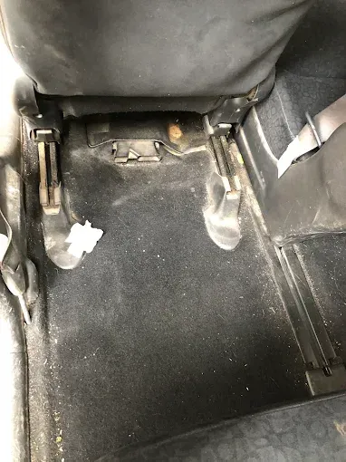 El suelo del coche está sucio detrás del asiento delantero, con un pequeño trozo de basura y los raíles del asiento 