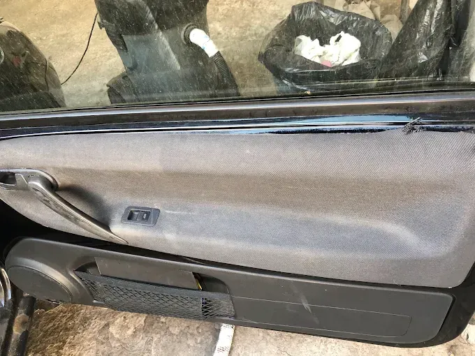 Primer plano del interior de la puerta de un coche con manija negra, moldura gris y ventana superior.
