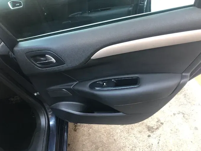 Interior de la puerta del coche con panel negro y gris, controles de ventanilla y manija de puerta plateada