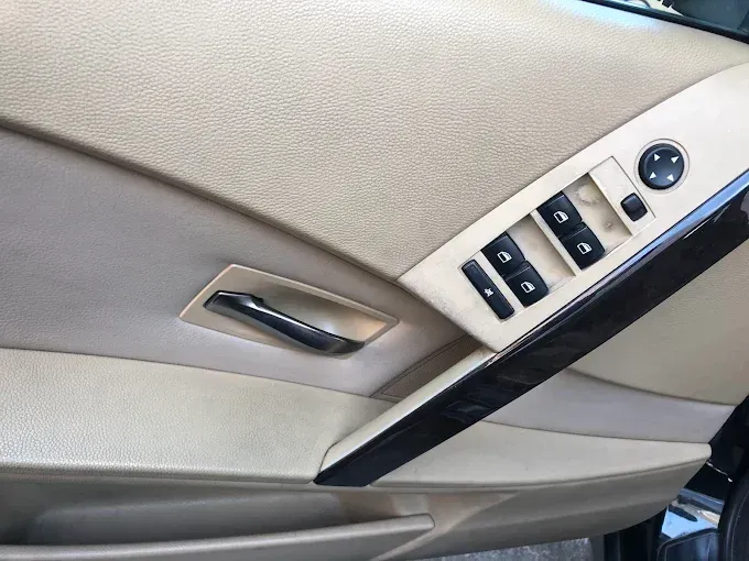 Interior de la puerta del coche con controles de ventanilla y cerradura en un panel beige y negro.
