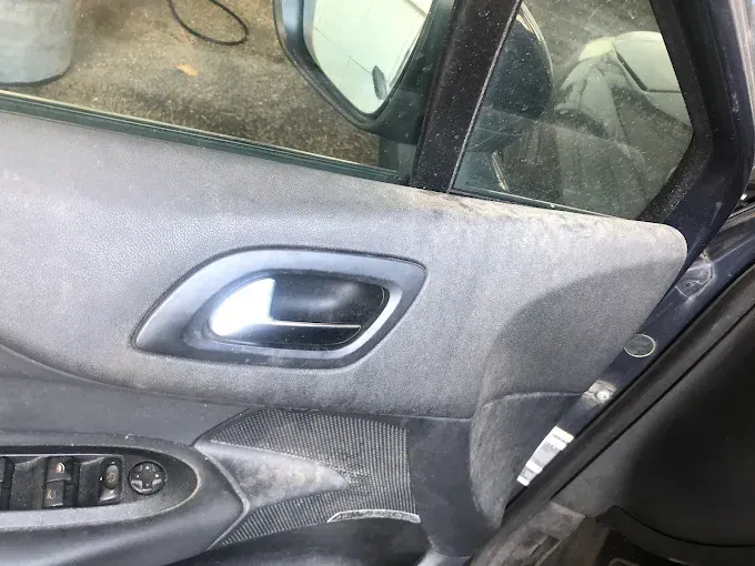 Interior de la puerta del coche con panel de tela gris, manija plateada y controles de elevalunas eléctricos.