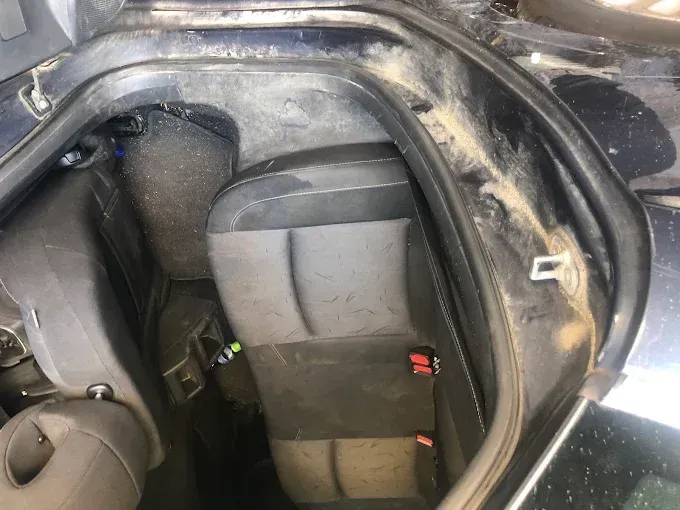 Dentro del maletero de un coche, una silla de coche gris para bebé está sujeta junto a una silla de coche negra para niño.