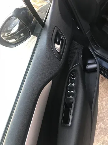 Interior de la puerta del coche con los controles de la ventanilla, la manija y el espejo lateral visibles.