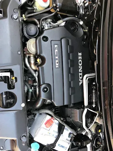 Compartimento del motor del coche con la cubierta de Honda, la batería y las mangueras visibles bajo el capó.