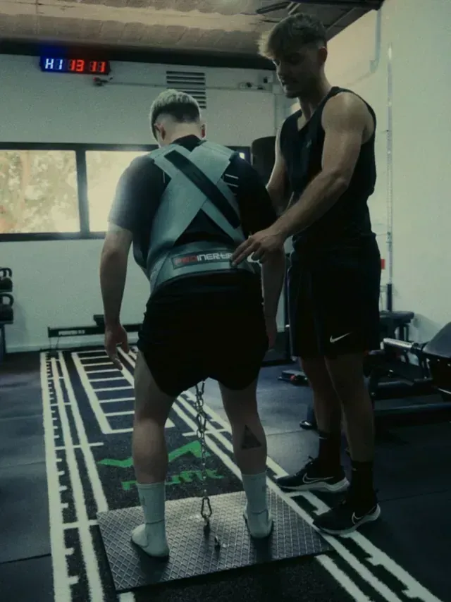 Un hombre que lleva un chaleco lastrado recibe ayuda de otro hombre en un gimnasio.