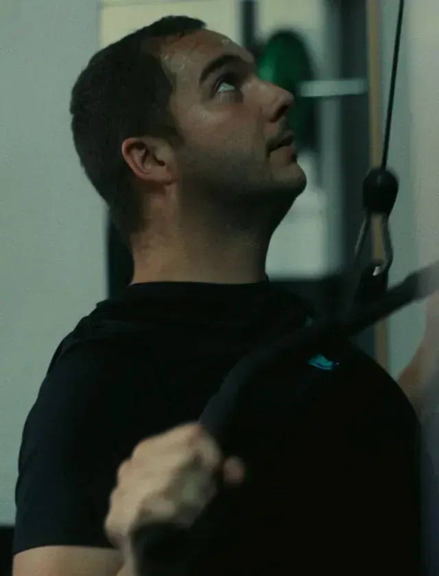 Un hombre con una camisa negra está usando una máquina en un gimnasio.