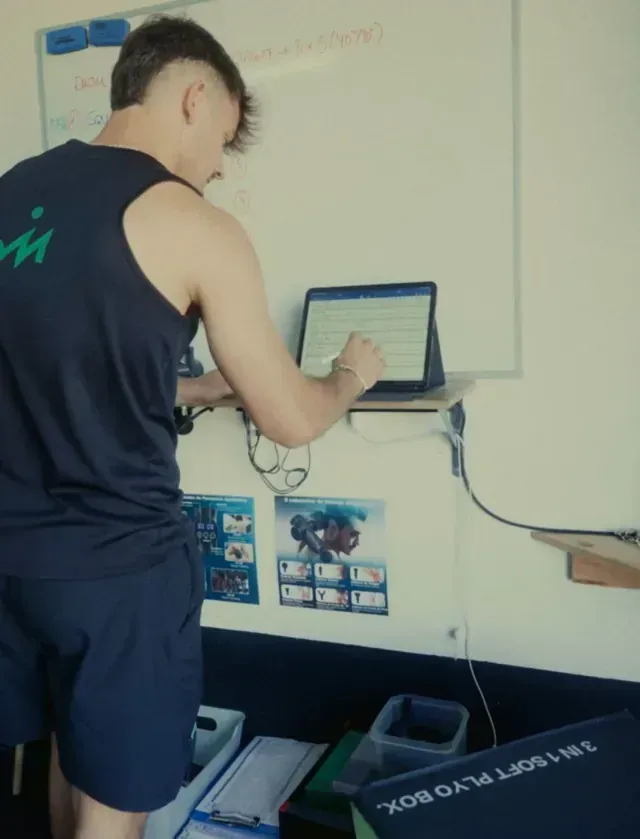 Un hombre con una camiseta sin mangas con la letra m en la espalda está trabajando en una computadora portátil.