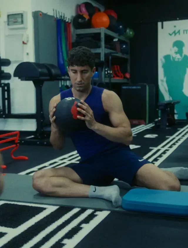 Un hombre con una camiseta azul sostiene un balón medicinal en un gimnasio.