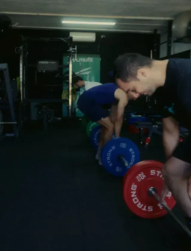 Dos hombres están levantando pesas en un gimnasio y una de las pesas tiene la palabra fuerte escrita en ella.