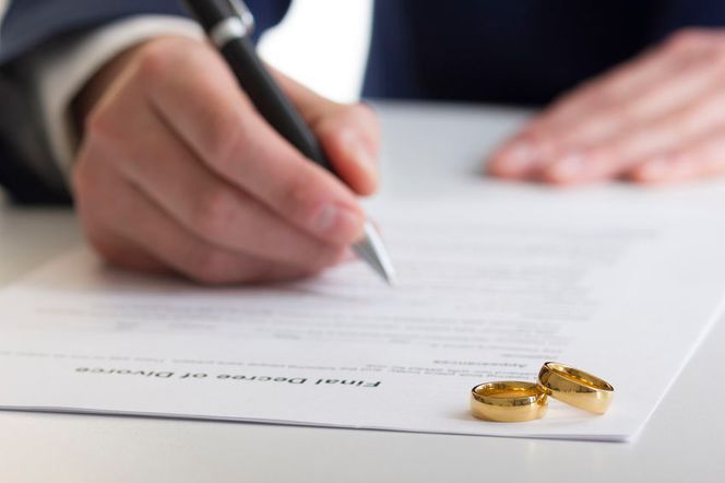 Un hombre está escribiendo en un trozo de papel al lado de un par de anillos de boda.
