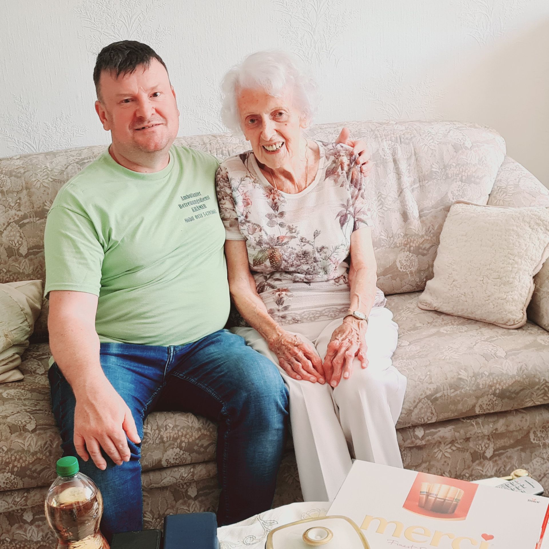 Ein Mann in einem grünen Hemd sitzt neben einer älteren Frau auf einer Couch