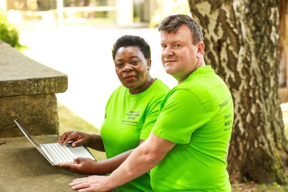 Zwei Personen in grünen Hemden schauen im Freien auf einen Laptop.