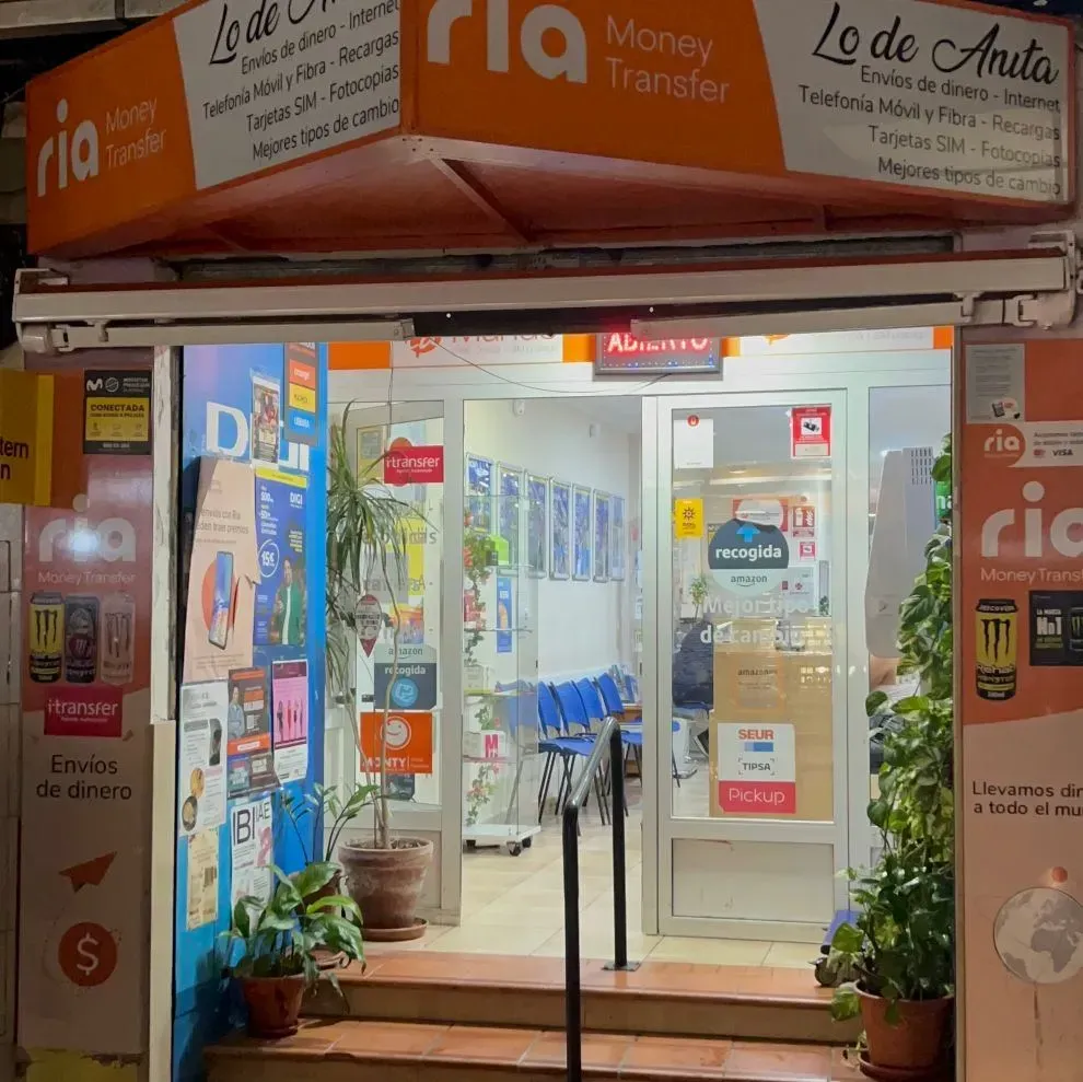 Escaparate de una tienda de transferencia de dinero Ria, con carteles, ventanas y plantas en macetas.