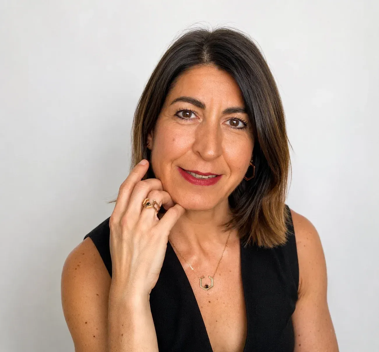 Mujer con cabello oscuro hasta los hombros, vestida con una blusa negra sin mangas, posando sobre un fondo blanco.
