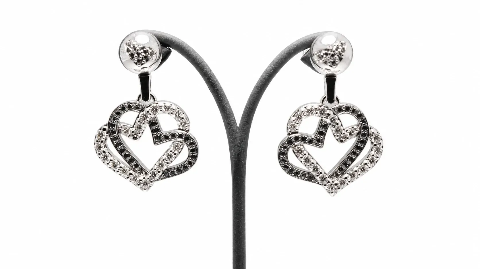 Pendientes de plata con forma de corazón y recortes en forma de estrella sobre un soporte de exhibición negro.