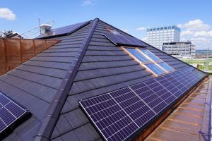 Dachterrasse mit Solarpaneelen und Oberlichtern vor blauem Himmel, im Hintergrund die Skyline der Stadt.