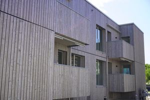 Aussenansicht eines modernen Gebäudes mit heller, vertikaler Holzverkleidung und Balkonen.