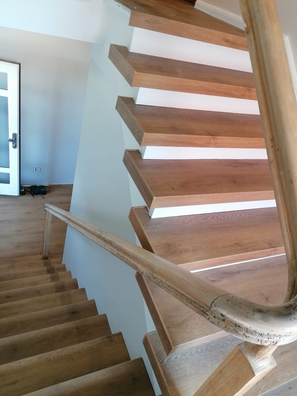 Holztreppe mit weißen Setzstufen, hellem Handlauf und Treppenabsatz neben einer weißen Wand.