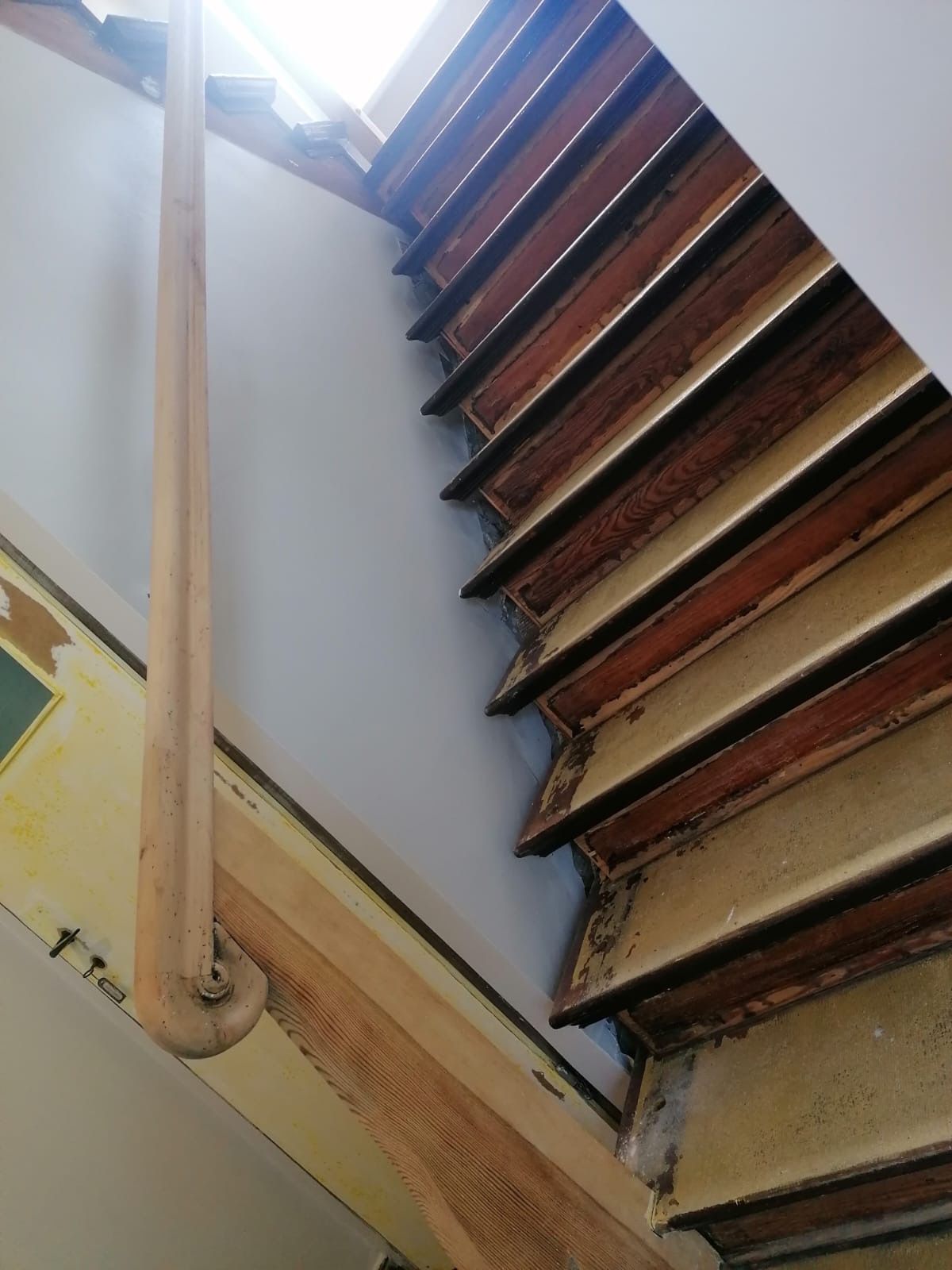 Holztreppe mit abblätternder Farbe, Geländer und Sonnenlicht von oben.