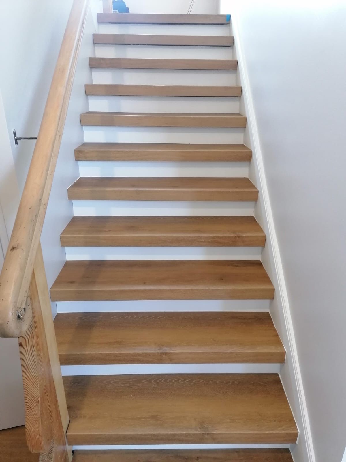 Holztreppe mit weißen Setzstufen und Holzhandlauf.