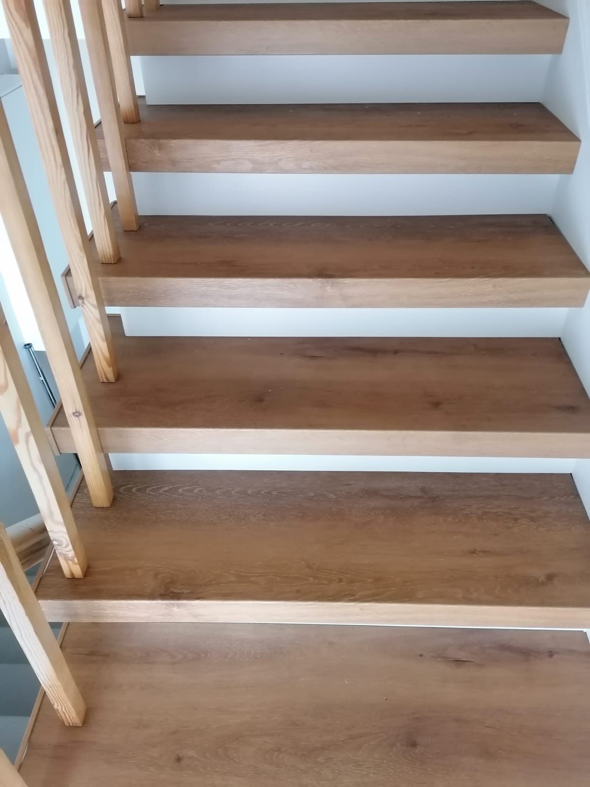 Holztreppe mit hellen Stufen und Geländer vor einer weißen Wand.