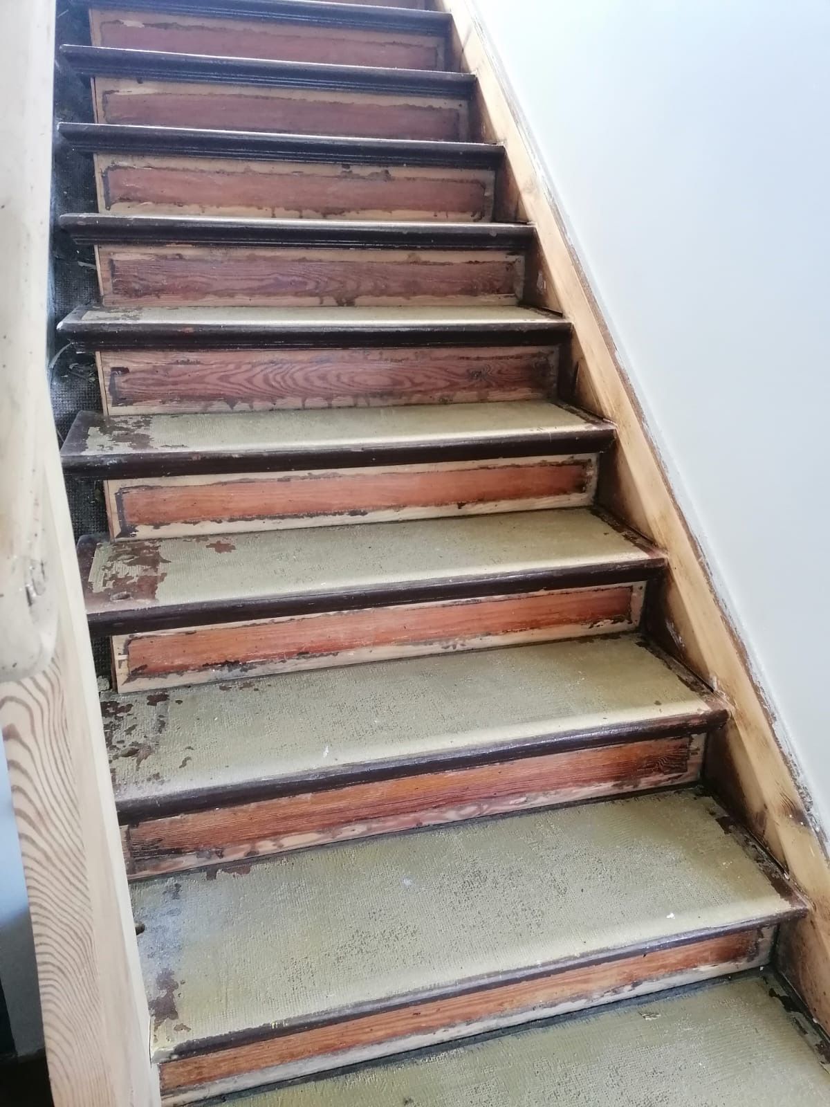 Holztreppe mit abblätternder Farbe und abgenutztem Teppich.