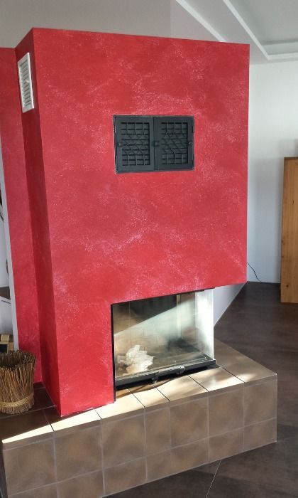 Roter Kamin mit schwarzer Entlüftung und Glasfeuerraum, auf Fliesensockel.