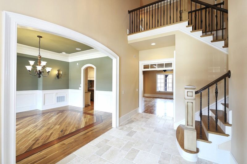 Innenansicht eines Hauses mit Treppe, Esszimmer und Eingangshalle. Holzböden, beige Wände und weiße Zierleisten.