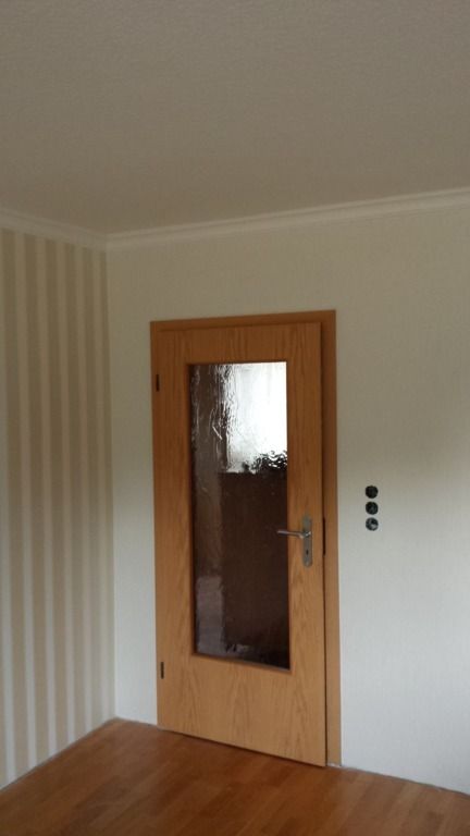 Holztür mit Glasplatte, in einem Raum mit hellen Wänden und einem Tisch.