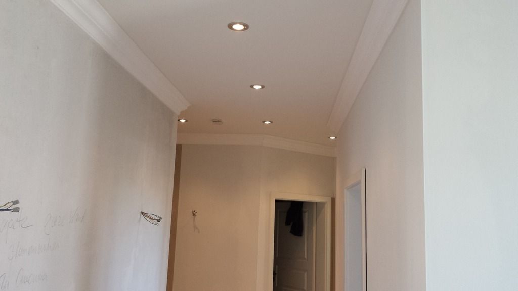 Ein Flur mit eingelassenen Deckenleuchten und Zierleisten, unfertigen Wänden und einer offenen Tür.