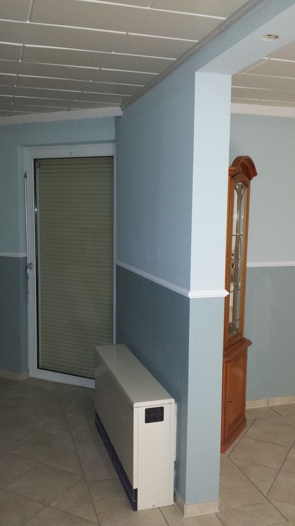 Zimmer mit blauen Wänden, einer weißen Tür mit Jalousien und einer großen Standuhr aus Holz.