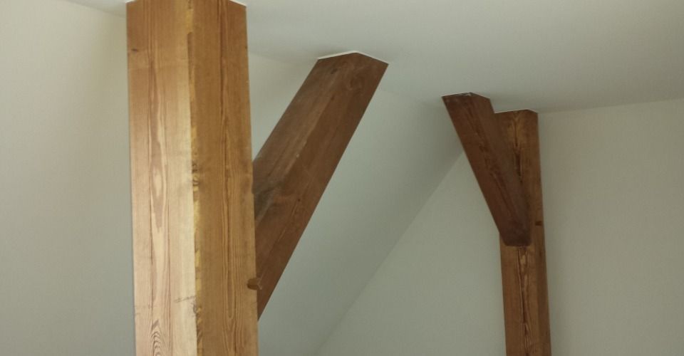 Holzstützbalken in einem Raum mit weißen Wänden, zwei schräg und einer vertikal.