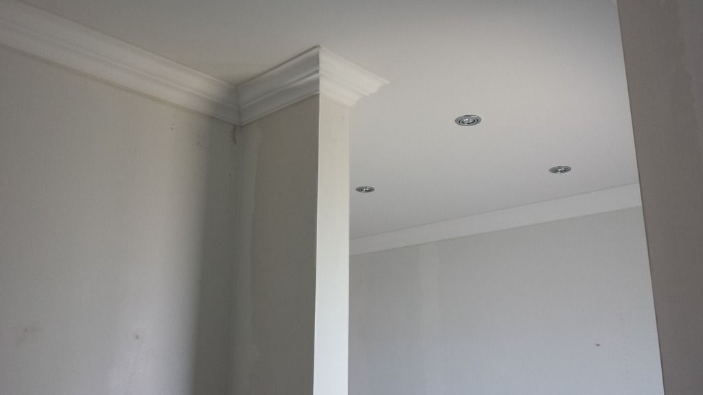 Weiße Zierleisten in einem Raum mit eingelassenen Deckenleuchten und grauen Wänden.